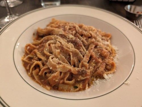 A plate of fettuccine pasta topped with a rich meat sauce and grated cheese.
