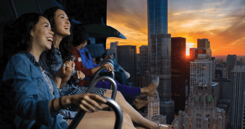 Two women enjoy a thrilling ride with a city skyline and sunset in the background, smiling and laughing together.