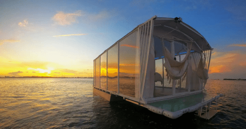 A modern floating house on water at sunset, featuring large glass walls and a serene atmosphere.