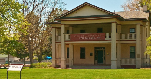 Chase Home Museum of Utah Folk Arts, a two-story building with a porch, surrounded by trees and green grass.