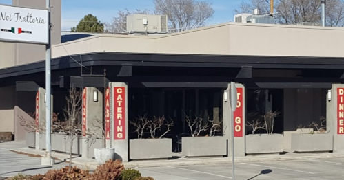 Exterior of a restaurant with signs for catering and to-go orders, featuring a modern design and outdoor seating.