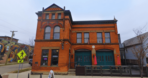 Historic brick building with large windows, a clock, and outdoor seating, featuring a brewery and pizzeria.