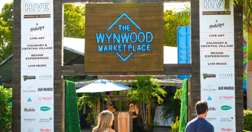 Entrance to The Wynwood Marketplace, featuring event signage and lush greenery. People walking in.