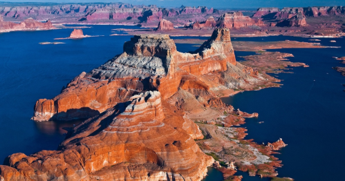 Aerial view of rugged red rock formations and blue water at Lake Powell, showcasing dramatic natural landscapes.
