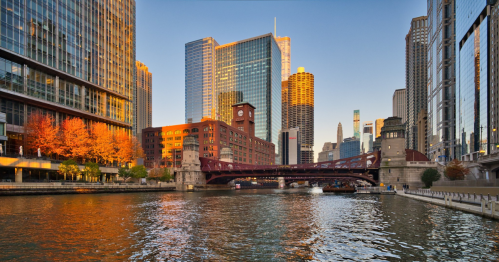 A scenic view of Chicago's skyline at sunset, featuring buildings, a bridge, and reflections on the river.