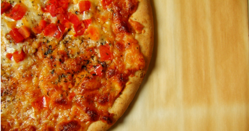 A close-up of a freshly baked pizza topped with melted cheese and diced tomatoes on a wooden surface.