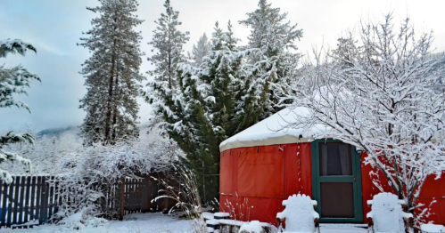 A cozy orange yurt surrounded by snow-covered trees and a winter landscape.