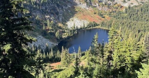 A serene mountain lake surrounded by lush green trees and rocky terrain, with colorful foliage in the background.