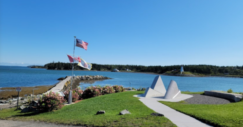 A scenic view of a coastal area with flags, a lighthouse, and a pathway along the water on a clear day.