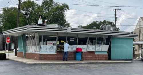 A retro-style fast food stand with large windows, a customer at the counter, and a "CASH ONLY" sign.