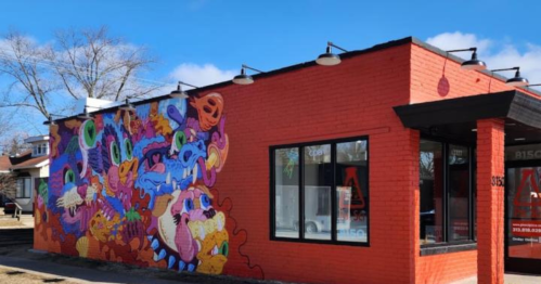Colorful mural on a red brick building featuring whimsical, cartoonish creatures and designs. Clear blue sky above.
