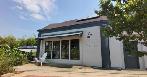 A charming storefront with large windows, a blue accent wall, and outdoor seating under a clear sky.