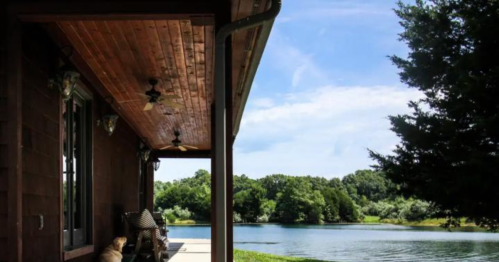 A peaceful lakeside view from a porch, featuring a dog resting and lush greenery in the background.