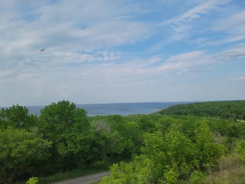 A scenic view of a lush green landscape meeting a calm blue lake under a partly cloudy sky.