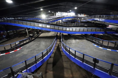 Aerial view of a go-kart track with multiple winding lanes and blue barriers under dim lighting.
