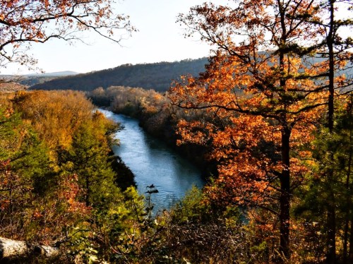 A serene river winds through a landscape of autumn trees, showcasing vibrant orange and yellow foliage.