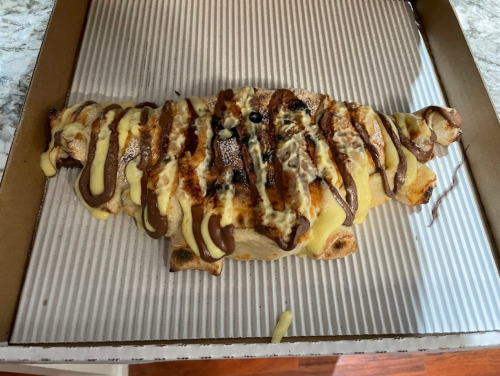 A large, baked pastry shaped like a croissant, drizzled with chocolate and cream icing, on a cardboard tray.