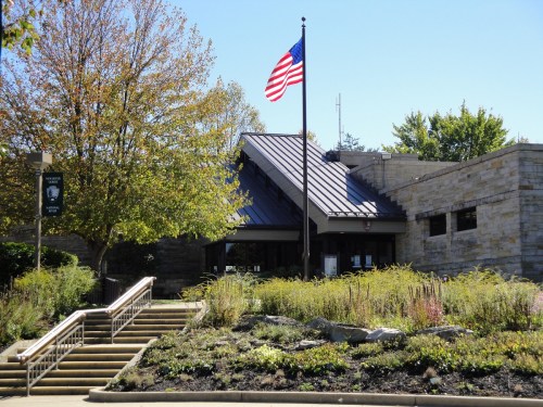A building with a stone facade, American flag, and landscaped garden, set against a clear blue sky.