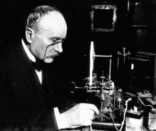 A man in a suit examines a vintage scientific instrument, focused on his work in a dimly lit room.
