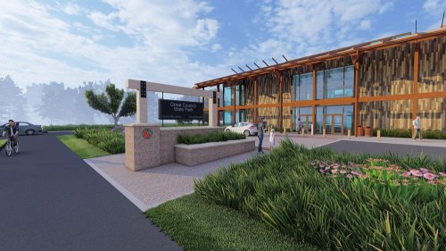 A modern building with wooden accents, surrounded by greenery and a sign for Grand Canyon State Park. Bicyclists nearby.
