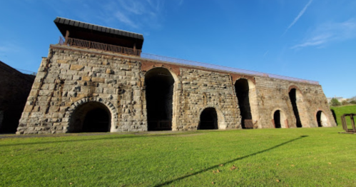 Historic stone structure with arched openings, set against a clear blue sky and green grass.