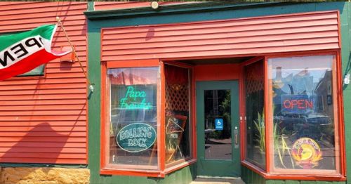 A colorful storefront with "Open" and "Papa D's" signs, featuring a flag and vibrant window displays.