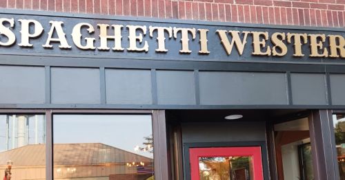 Sign for "Spaghetti Western" restaurant, featuring gold lettering on a dark background above a red door.