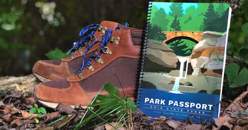 A pair of hiking boots next to an Ohio State Parks passport booklet, set against a natural background.