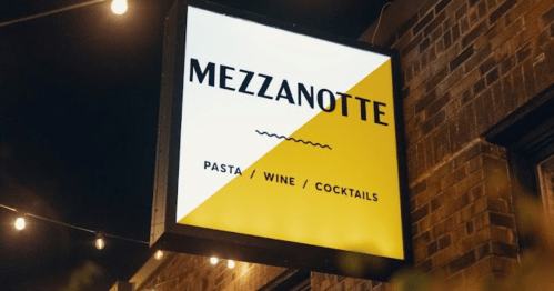 Sign for "Mezzanotte" featuring a yellow and white design, advertising pasta, wine, and cocktails.