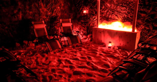 A cozy, dimly lit room with red lighting, featuring lounge chairs and a glowing salt rock display.