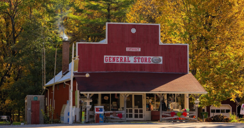 A charming red general store surrounded by vibrant autumn trees, with smoke rising from the chimney.