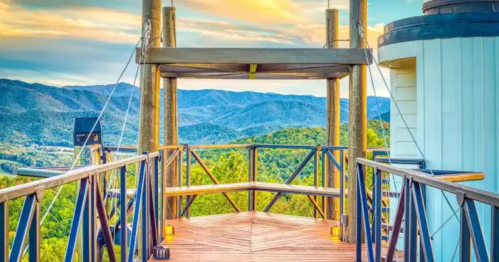 A wooden observation deck with a scenic view of mountains and a colorful sky at sunset.