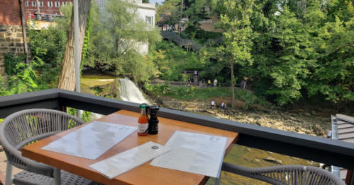 A scenic view from a restaurant table overlooking a waterfall and lush greenery. Menus and condiments are on the table.