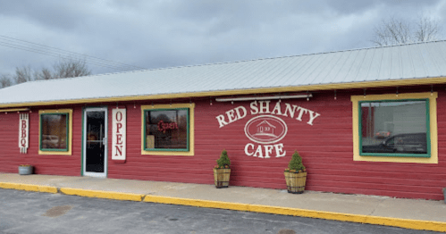 A red wooden building with a sign reading "Red Shanty Cafe" and an "Open" sign in the window. Cloudy sky above.