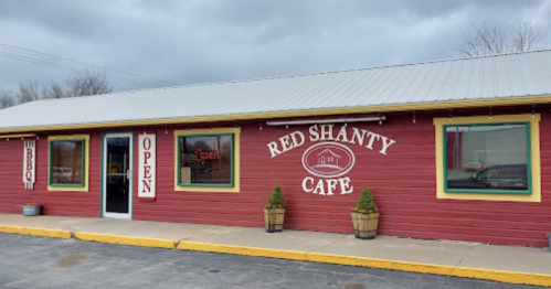 A red wooden building with a sign reading "Red Shanty Cafe" and an "Open" sign in the window. Cloudy sky above.