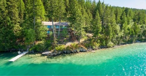 A serene lakeside view featuring a house surrounded by lush trees and clear turquoise water.