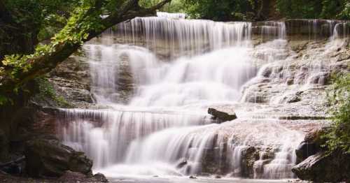 A serene waterfall cascading over rocky ledges, surrounded by lush greenery and trees.