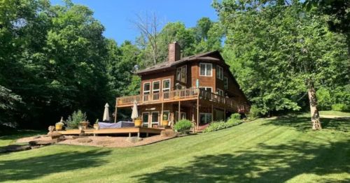 A large wooden house surrounded by lush greenery and a well-maintained lawn on a sunny day.
