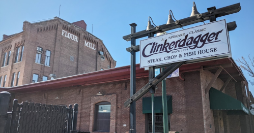 Sign for Clinkerdagger restaurant in front of a historic brick flour mill building under a clear blue sky.
