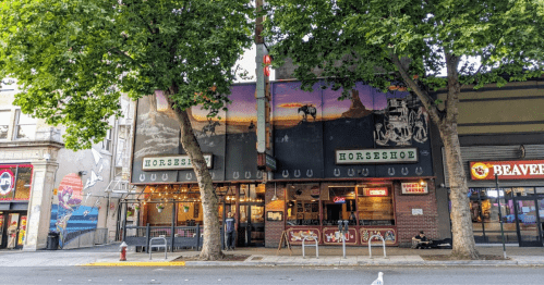 A storefront of the Horseshoe restaurant, featuring large windows and a mural, surrounded by trees and city streets.