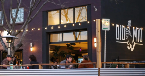 Outdoor dining scene at a restaurant with string lights, featuring patrons enjoying their meals on a patio.