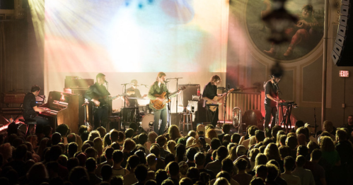 A live band performs on stage with colorful lights, while a large audience enjoys the show.