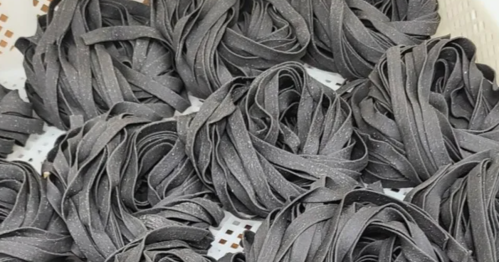 Bundles of dark gray pasta arranged in a basket, showcasing their twisted, ribbon-like shapes.