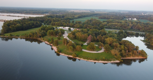 Aerial view of a lush green island surrounded by calm water, with trees and a winding path visible.
