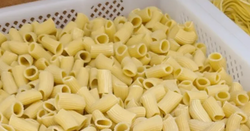 A close-up of uncooked pasta shapes, specifically short, ridged tubes, in a white basket.