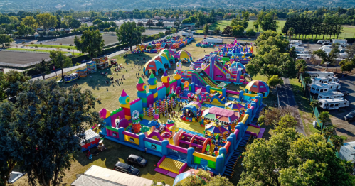 Aerial view of a colorful inflatable amusement park with various bounce houses and attractions in a green landscape.