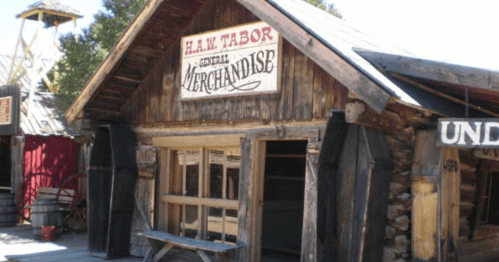 A rustic wooden storefront with a sign reading "H.W. Tabor General Merchandise" in a western-style setting.