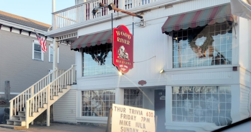 Exterior of Wood River Bar & Grill with a sign advertising trivia night and live music schedule.