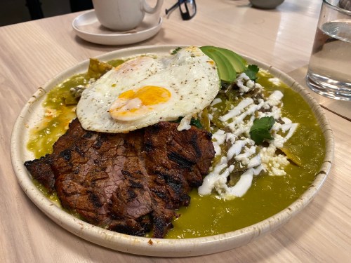 A plate of grilled steak topped with two fried eggs, avocado, cheese, and green sauce, served with rice and beans.