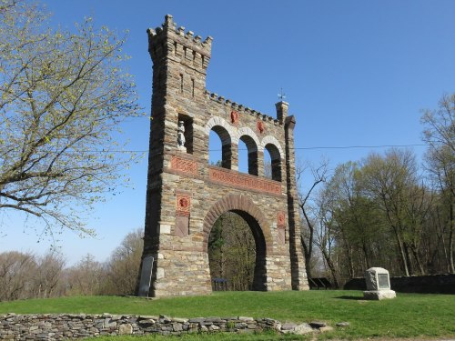 A stone archway structure with decorative elements, surrounded by trees and a clear blue sky.